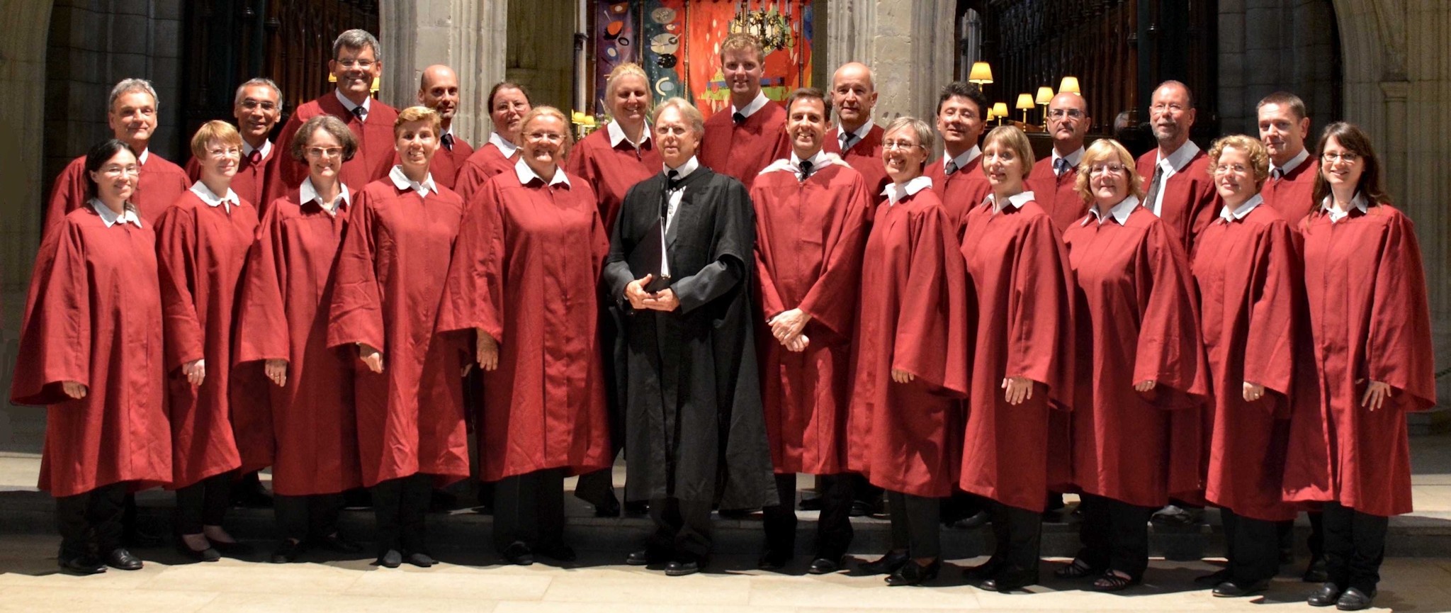 A mixed quoir, in red robes, with its conductor in a black robe.