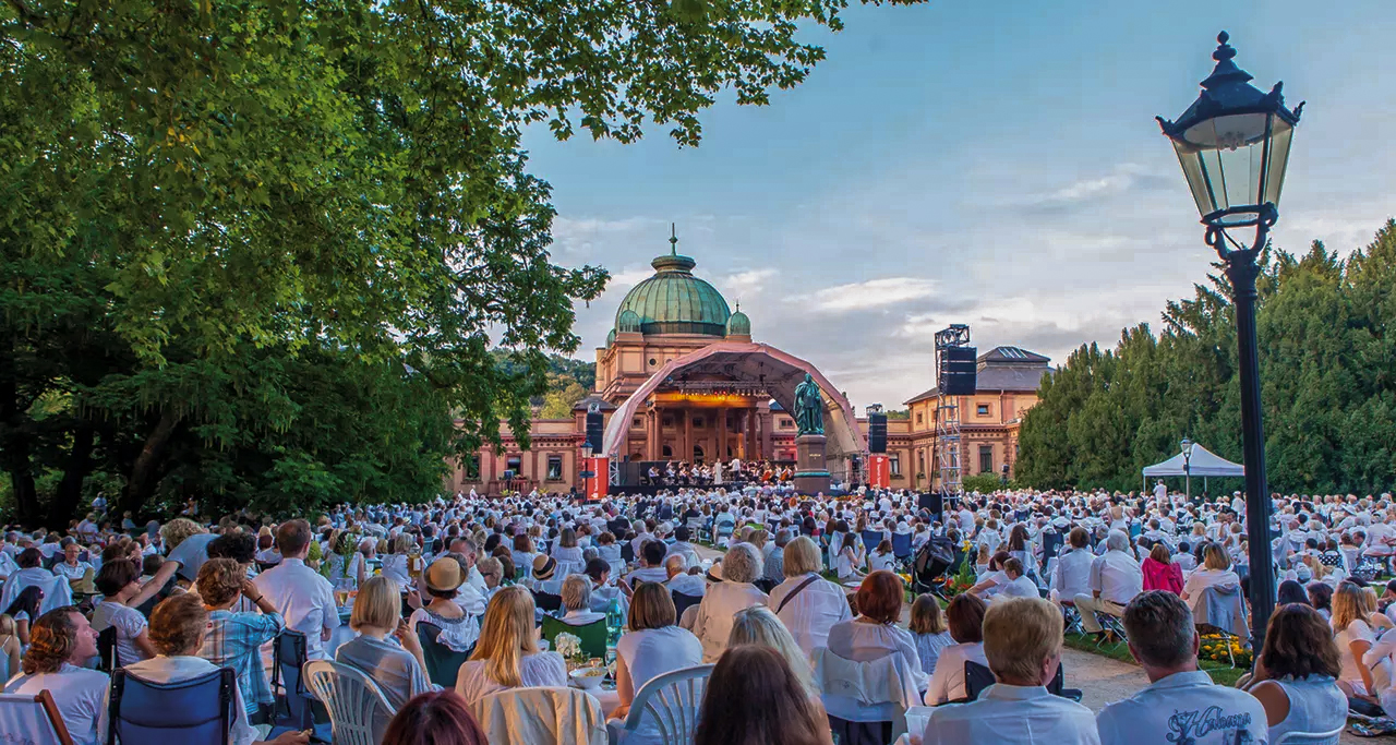 A large crowd of people, all wearing white, in front of a concert stage at Bad Homburg Kurpark