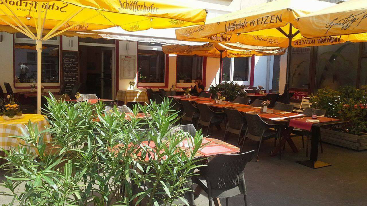 The outdoors beer garden of the Lilium restaurant in Frankfurt-Bockenheim with an olive bush in the foreground.