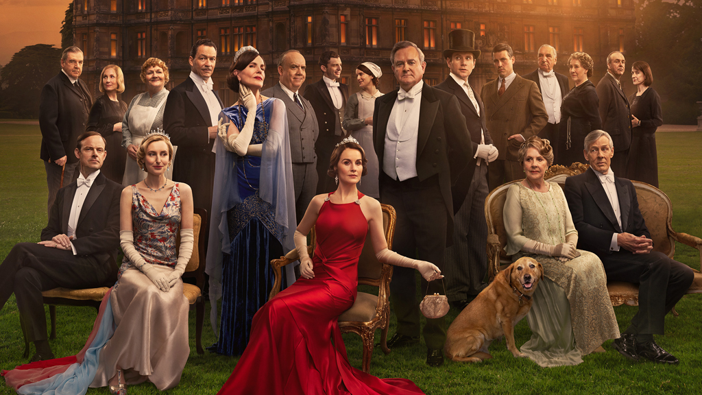 A large group of people have gathered for a photograph in front of a grand mansion at sunset.